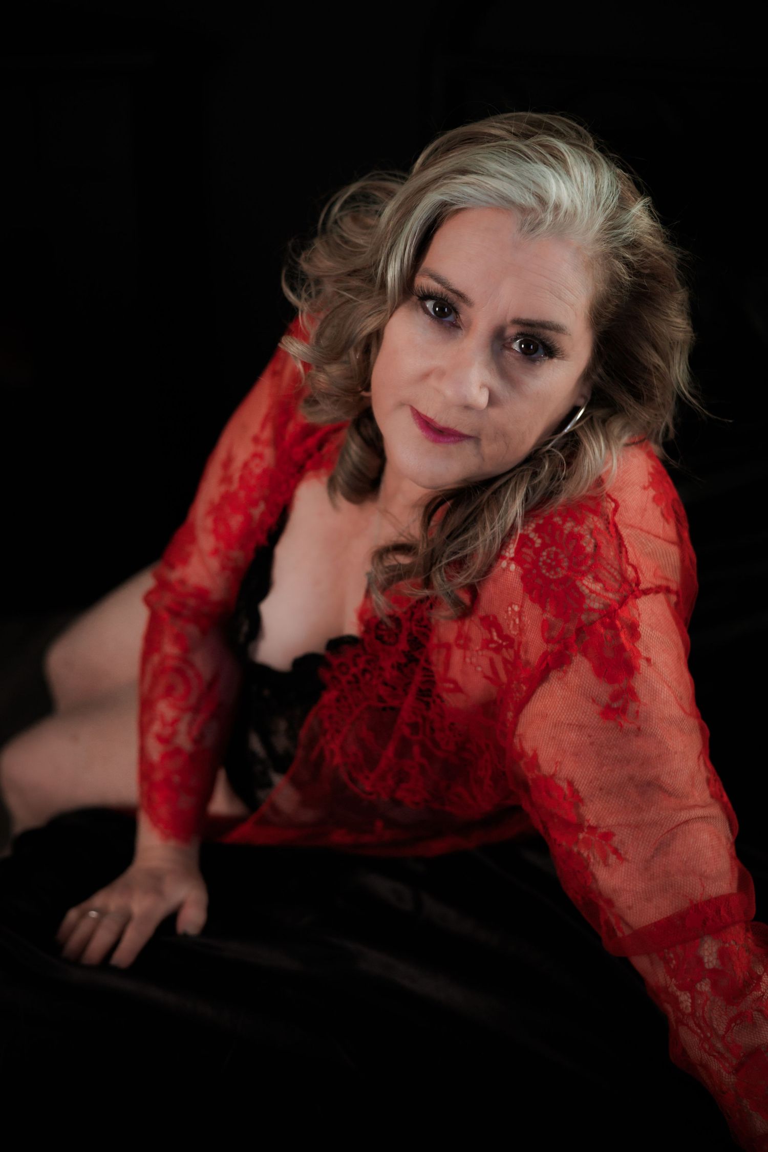 Glamour portrait of woman in red lace top against dark background.
