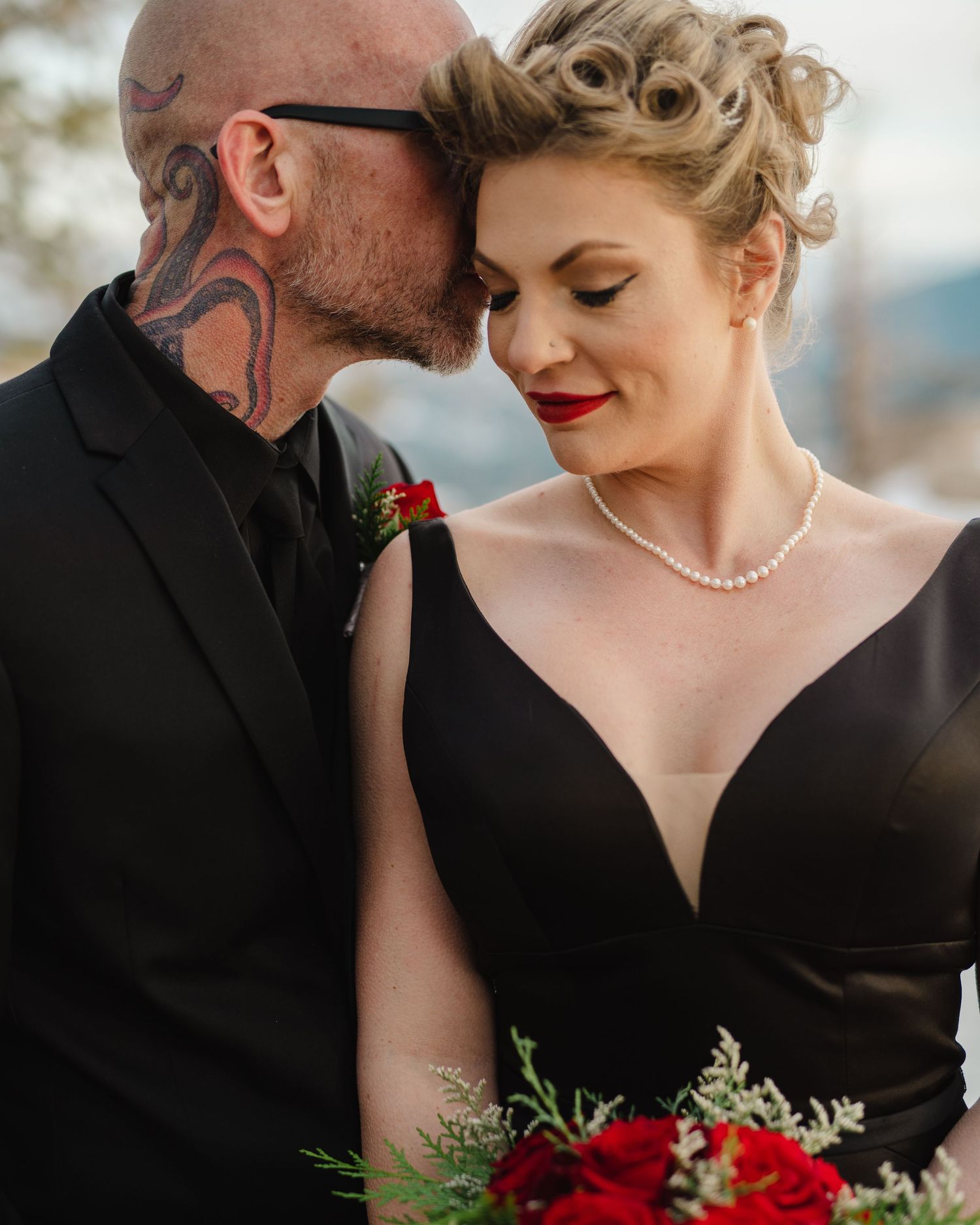 A romantic wedding portrait featuring an elegant couple in black attire with red roses.
