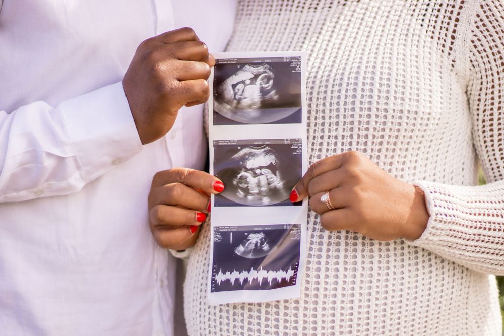 Hands holding ultrasound photos showing baby's development stages.