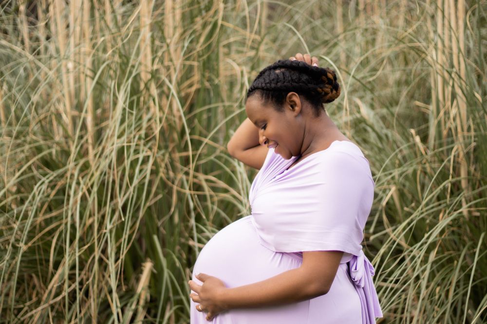 Maternity photo in soft pink dress against tall grasses.