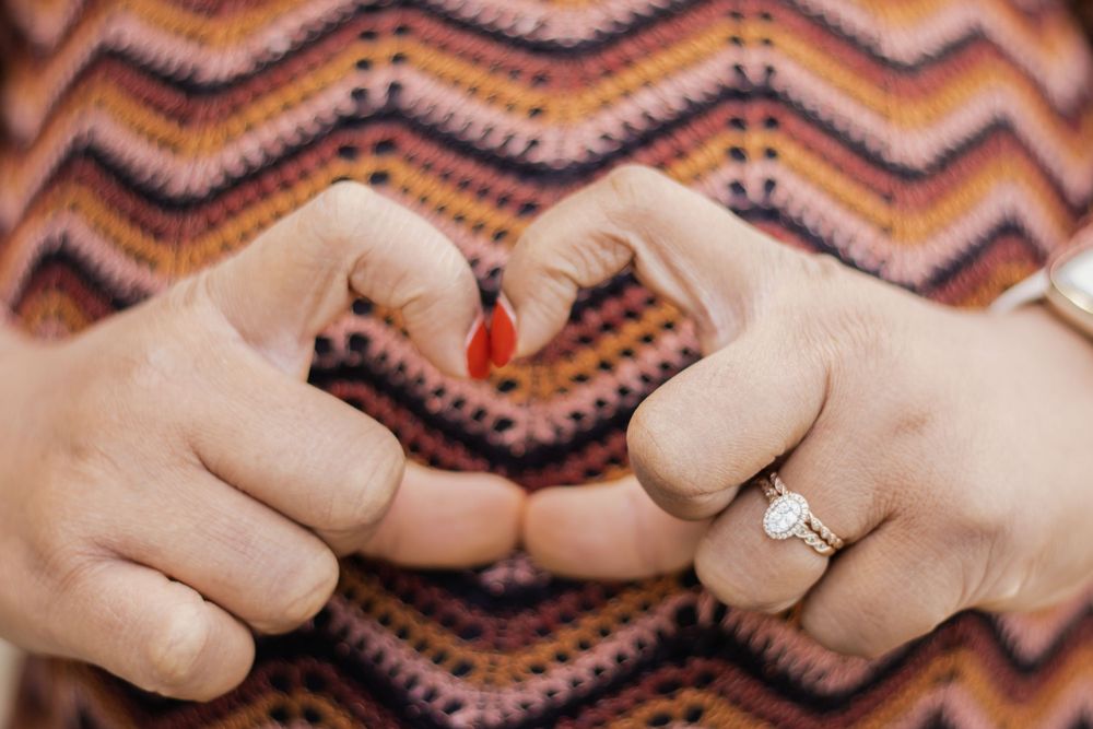 Hands wearing an engagement ring against a colorful chevron patterned background.
