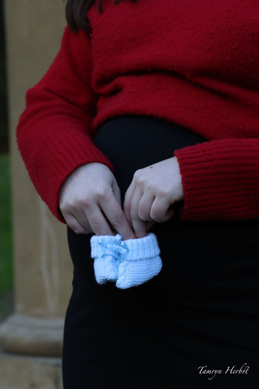 A pregnant woman holds blue baby booties