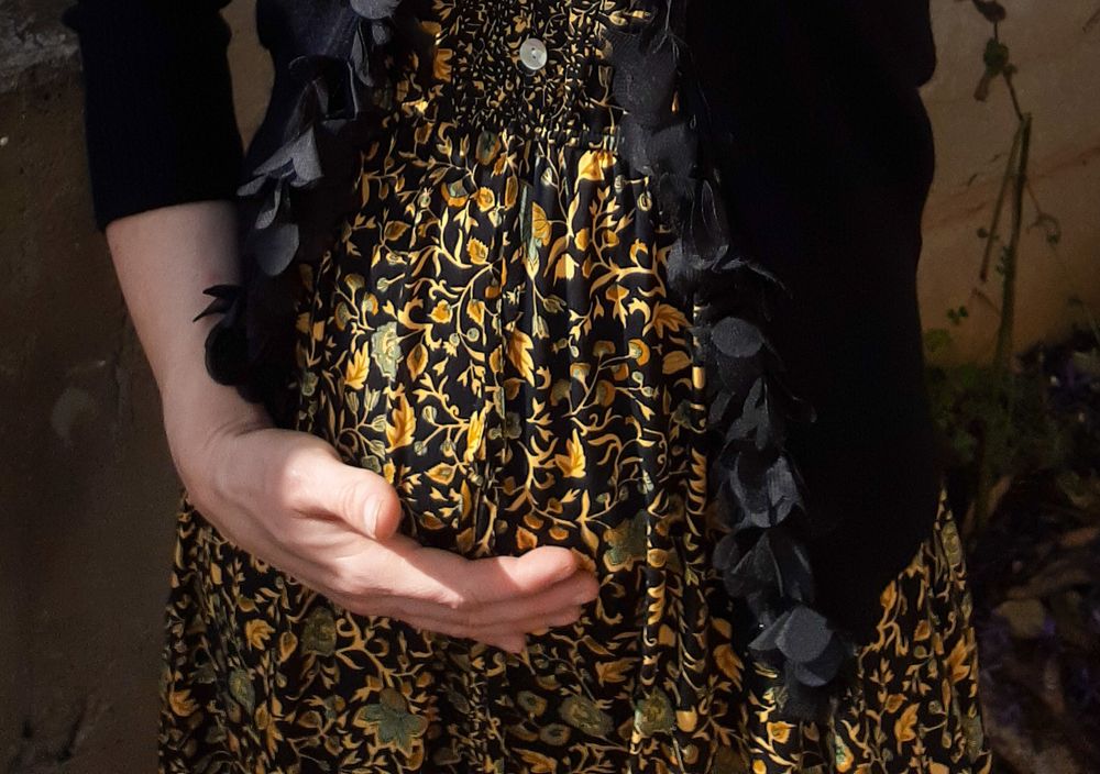 Hands cradling belly against dark floral patterned dress in moody lighting.