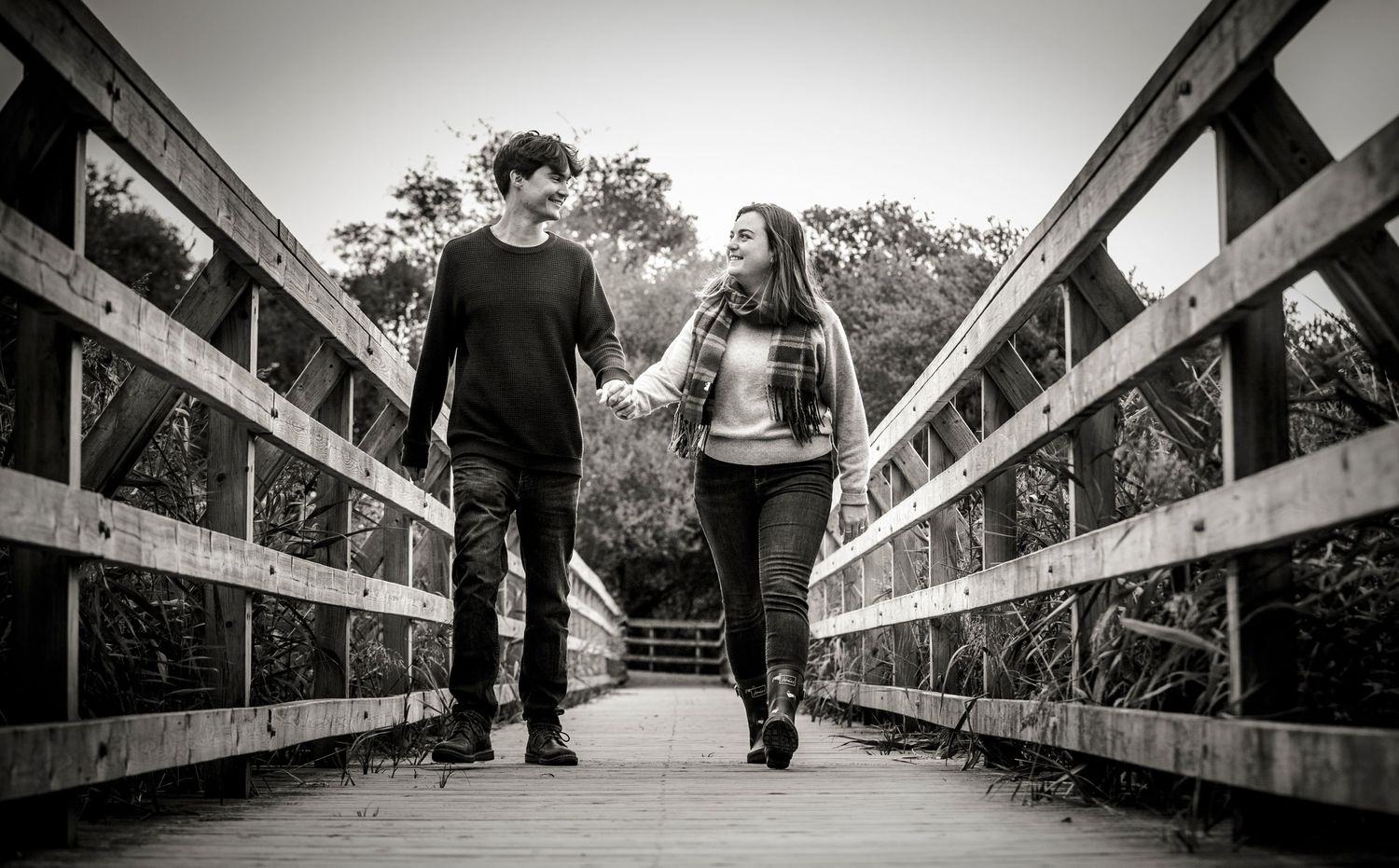 People walking along a wooden boardwalk bridge in black and white.
