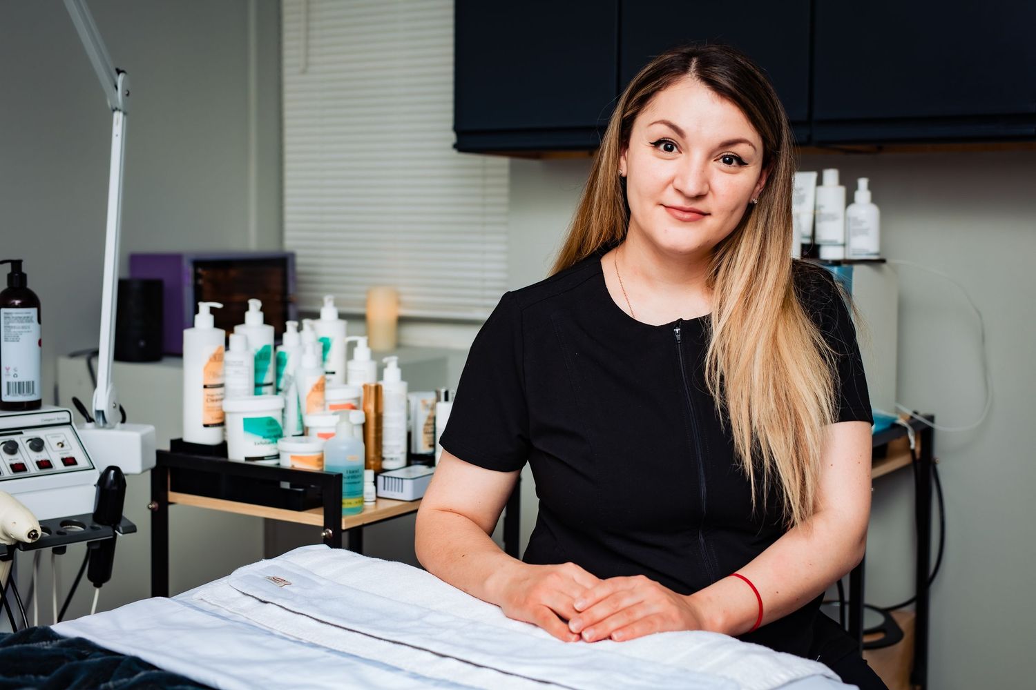 Professional photo of cosmetologist at workstation with beauty products in background.