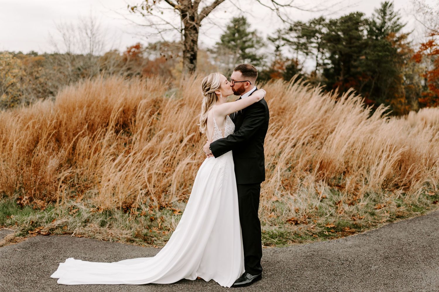 A wedding couple shares an intimate moment on a path surrounded by golden autumn grasses.