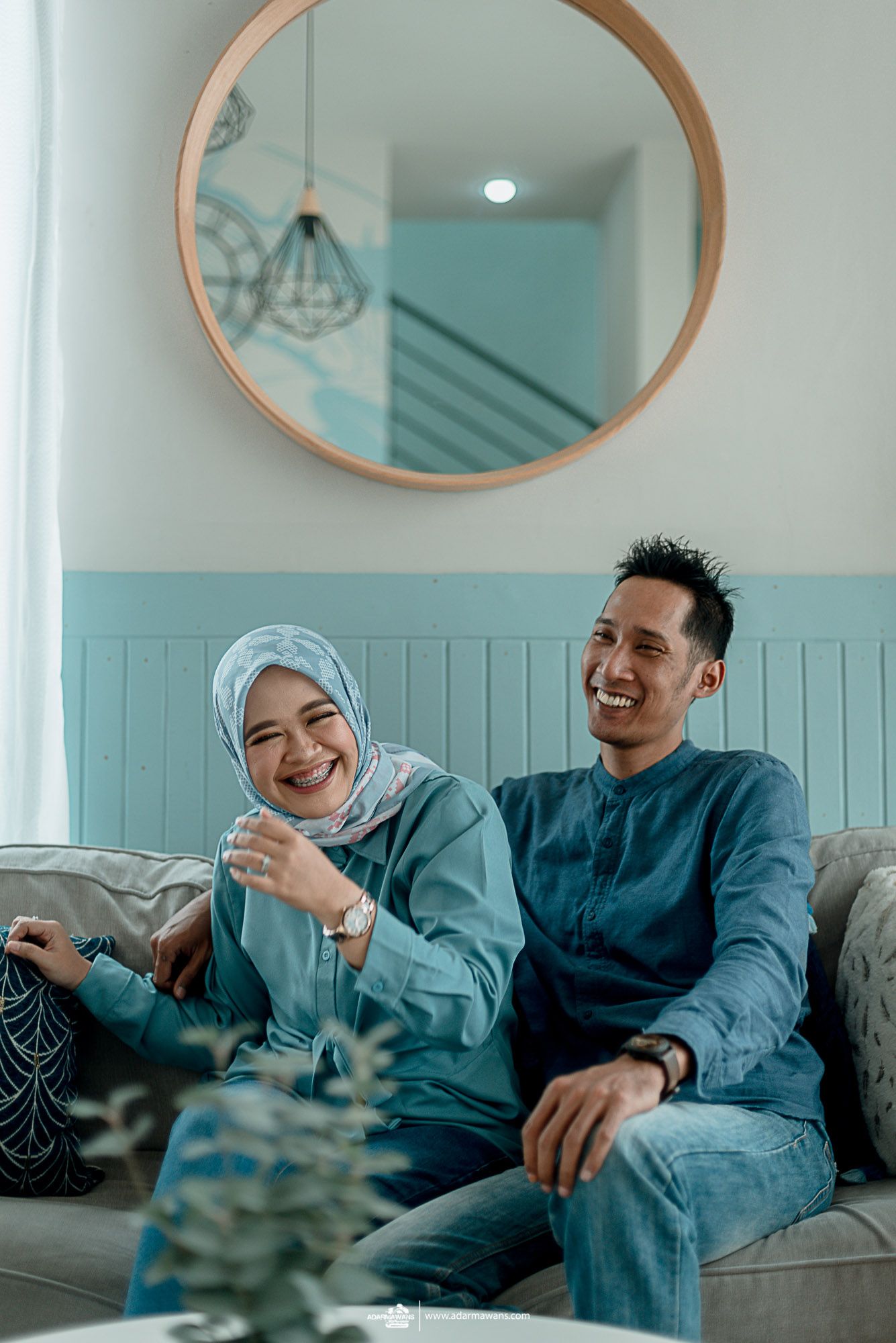 Couple sharing joyful moment on grey couch with round mirror and mint wall decor.