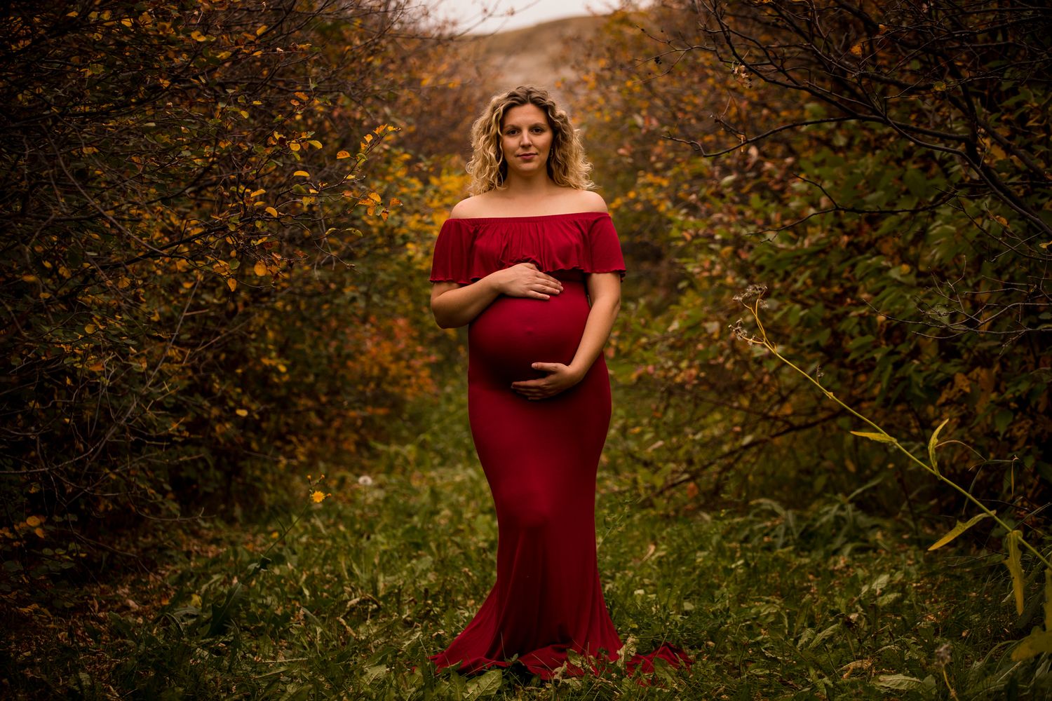 Maternity photo of woman in red dress during autumn outdoor session.