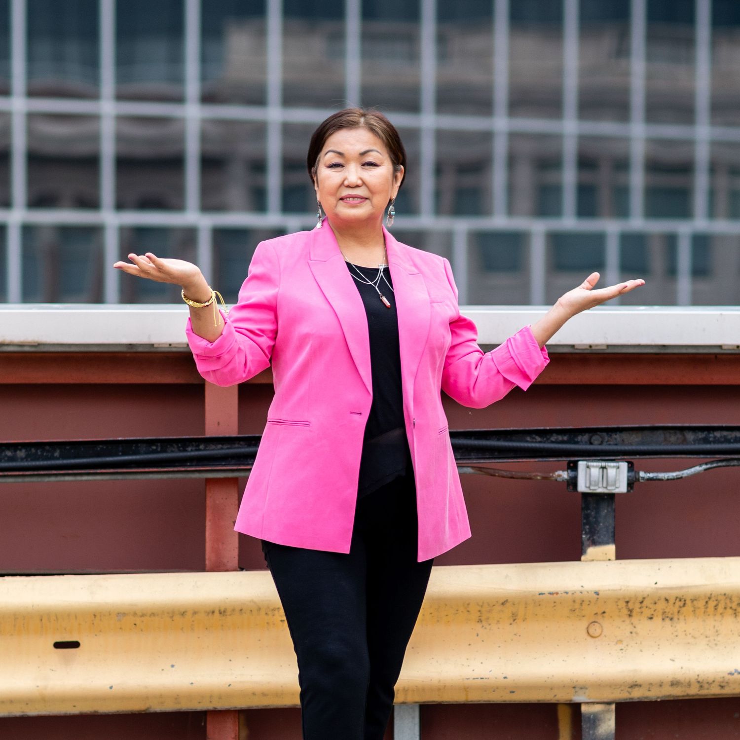 Professional outdoor portrait in bright pink blazer against urban backdrop.