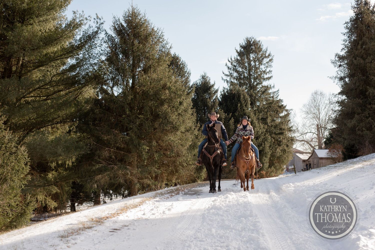 Two riders on horseback traverse a snow-covered trail through a pine forest.