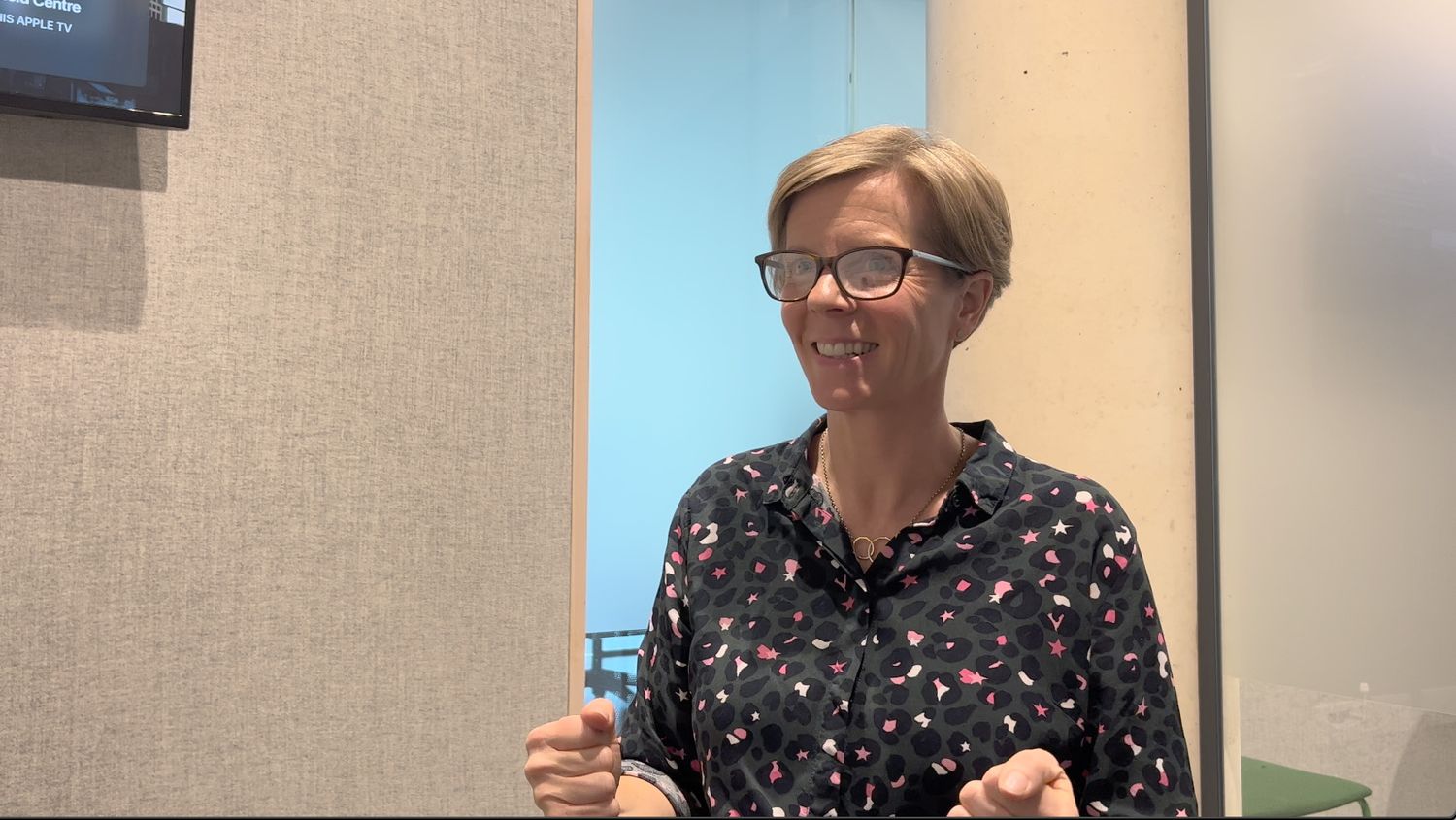 mature white woman sitting in a room talking and smiling wearing a patterned top