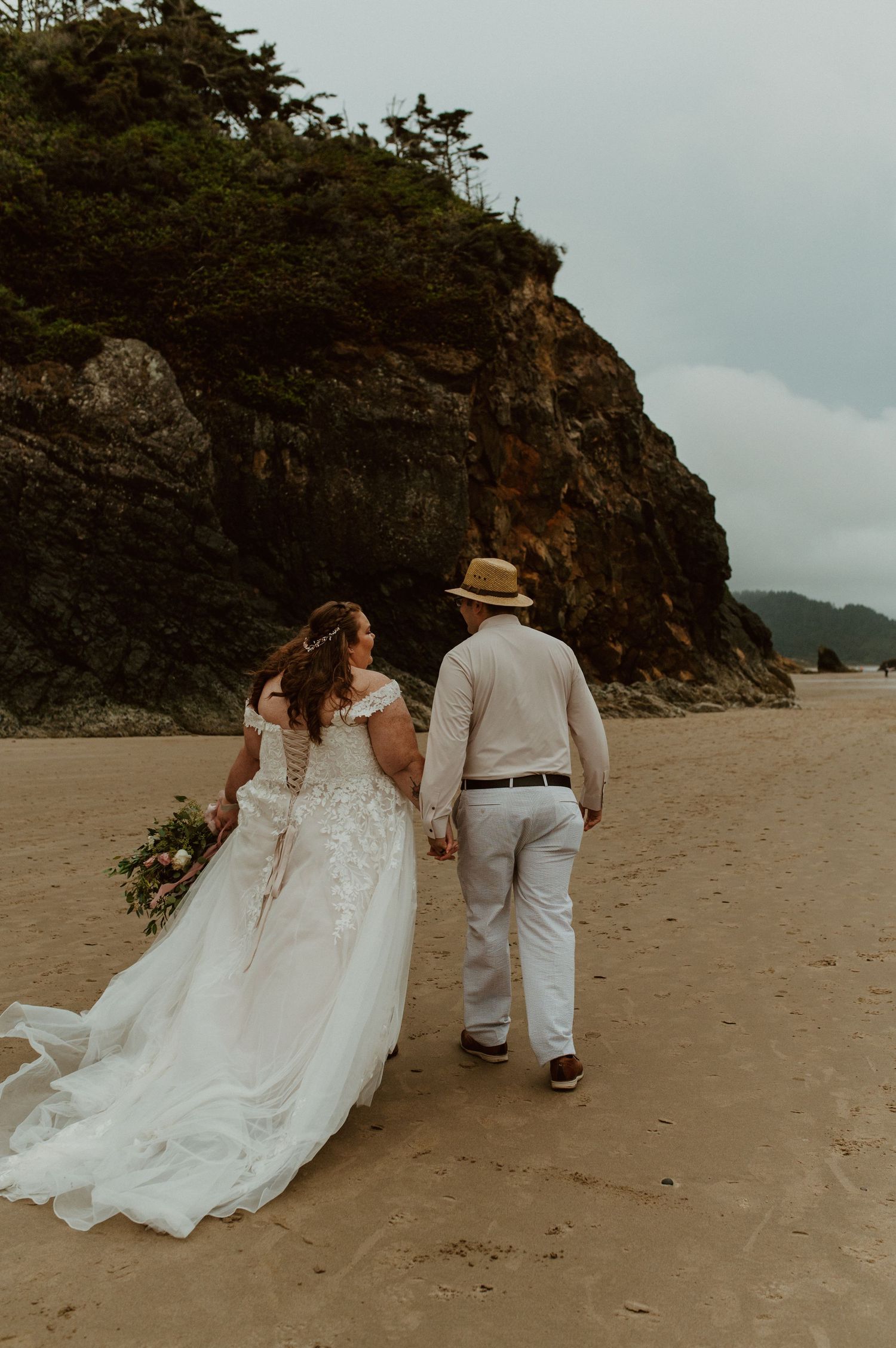 Beach wedding photos with rocky cliffs and overcast sky.