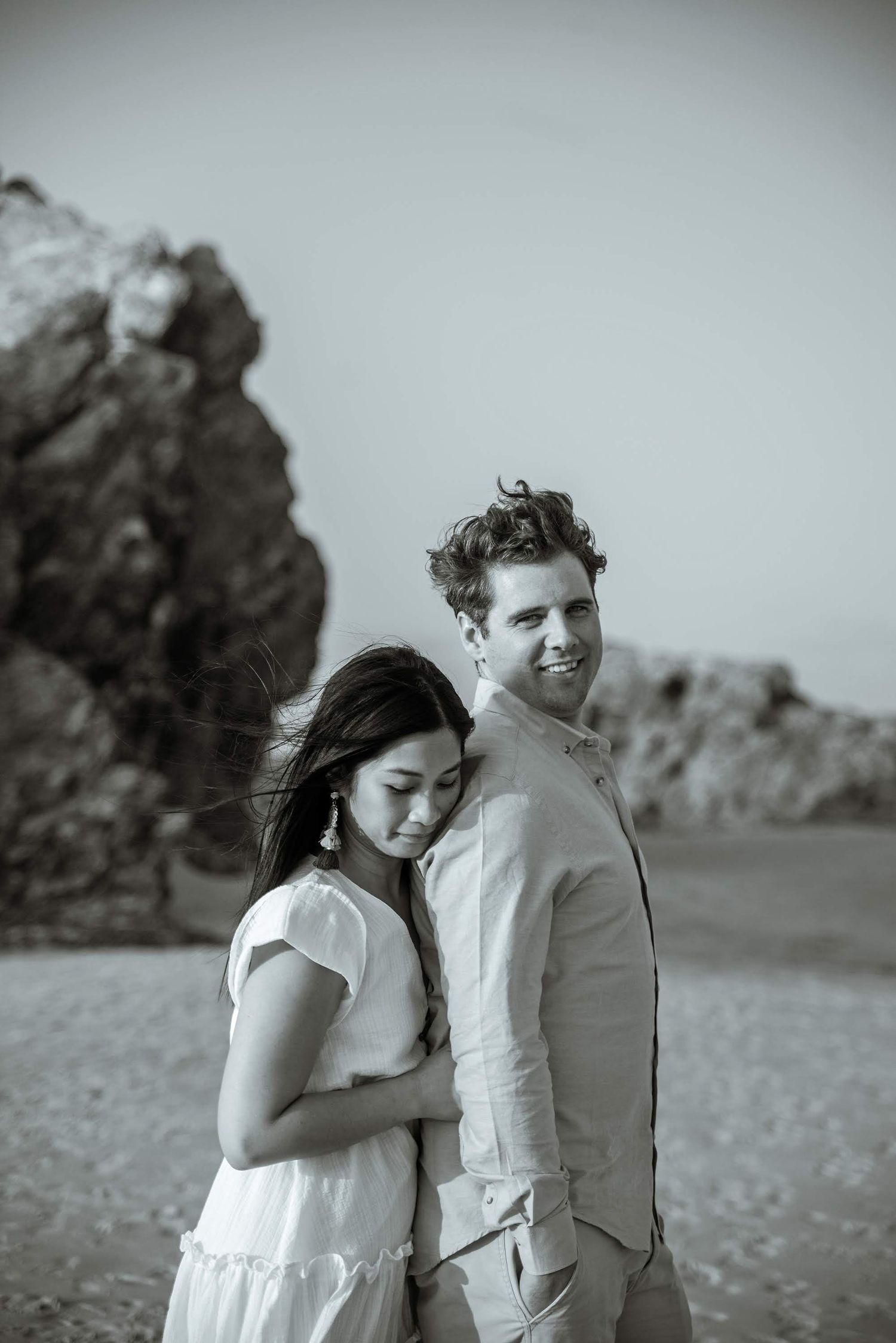 A romantic black and white portrait of a couple against rocky coastal backdrop.