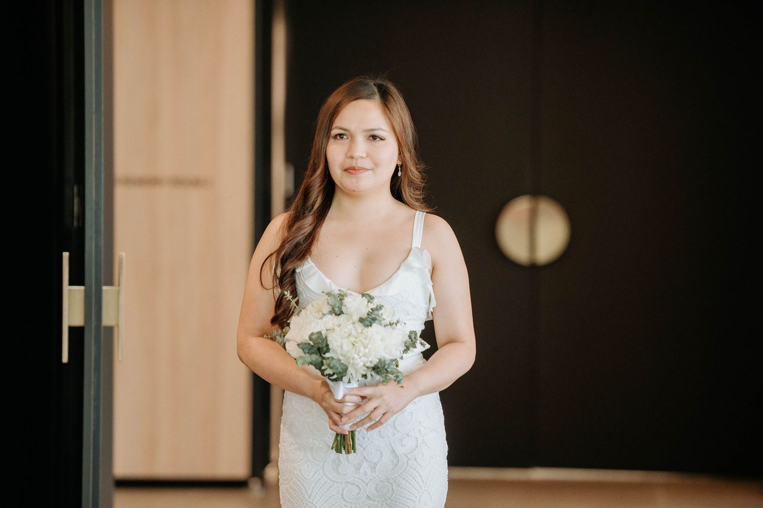 A bridal portrait showing a lace dress and white floral bouquet in a natural light setting.