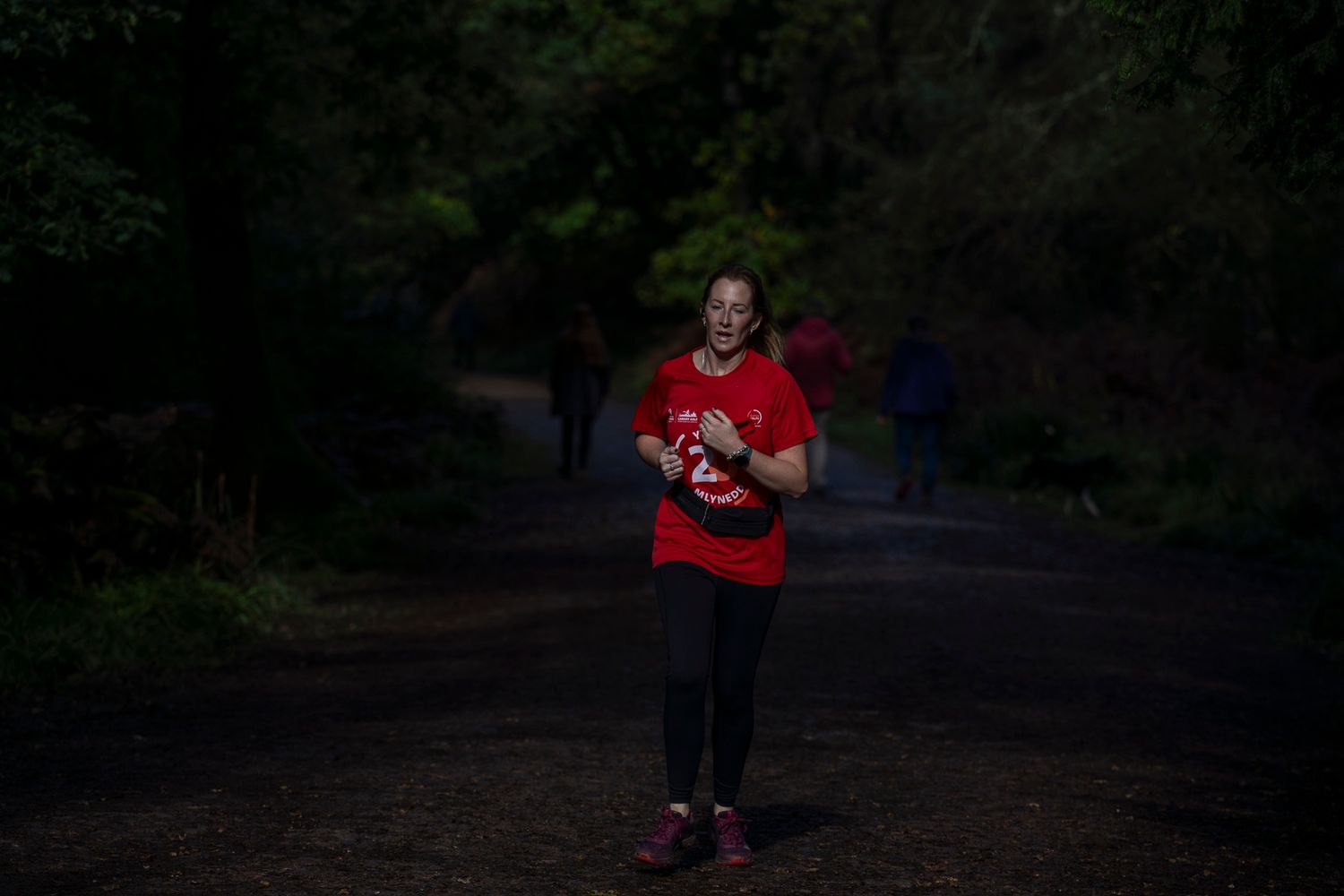 A jogger illuminated by evening light running through a dark wooded path.