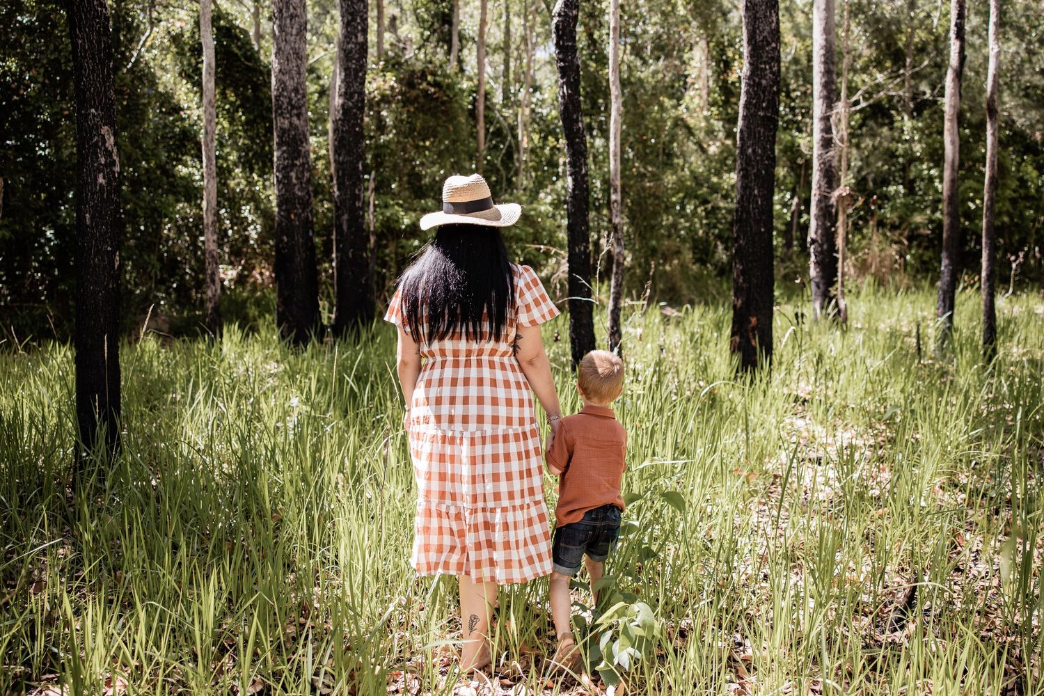 Adult and child walking together through a sun-dappled eucalyptus forest.