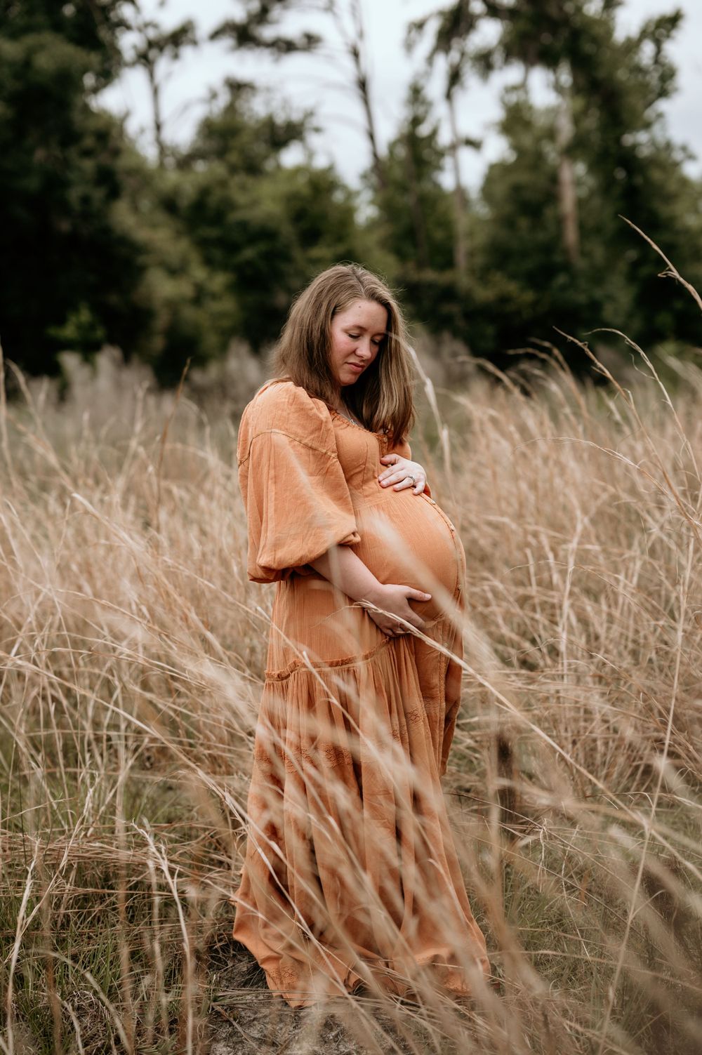 Artistic maternity photo in rustic dress amid golden field of tall grass.