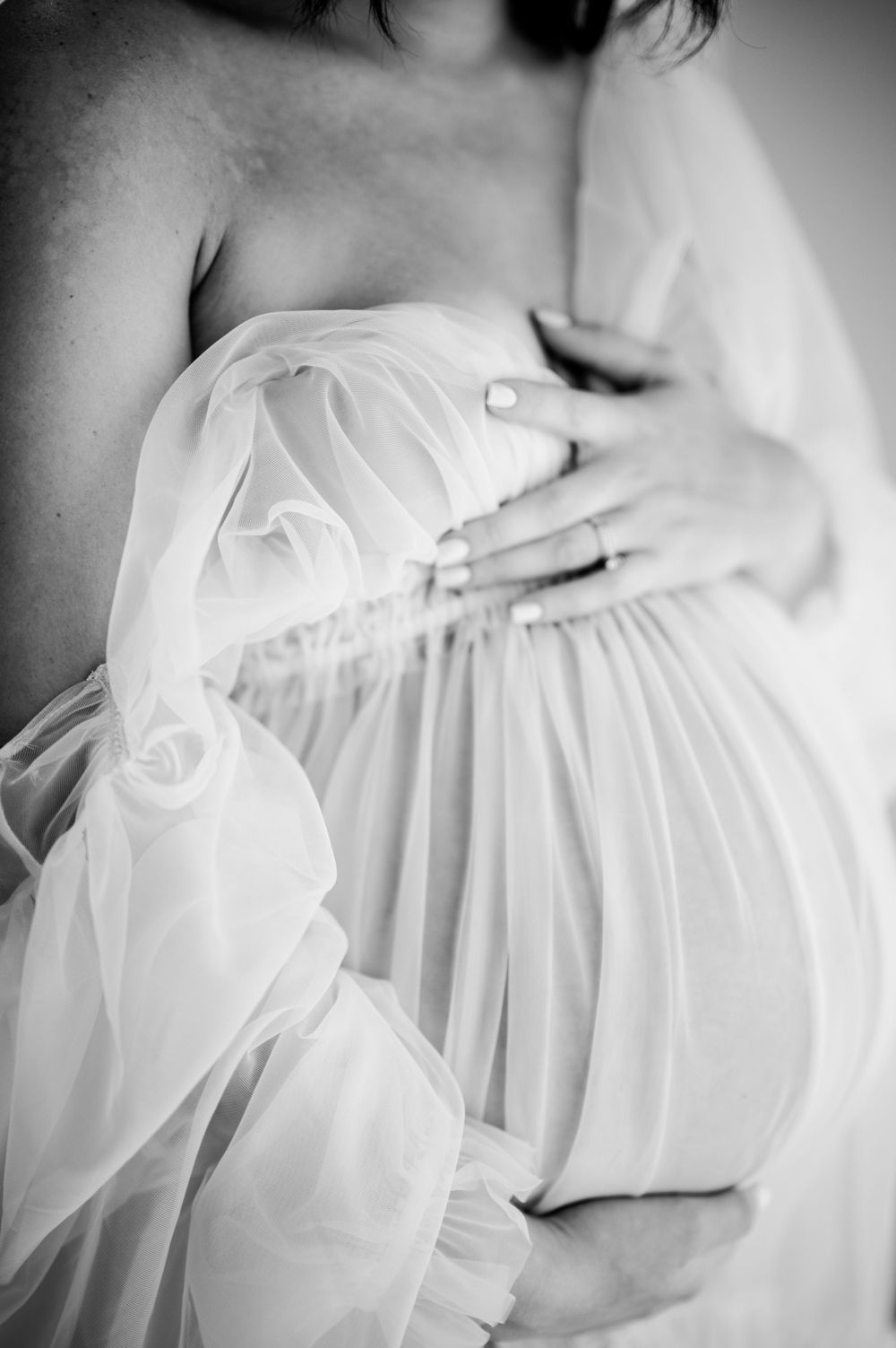 Black and white artistic photo of pregnancy with draped sheer fabric highlighting the baby bump.
