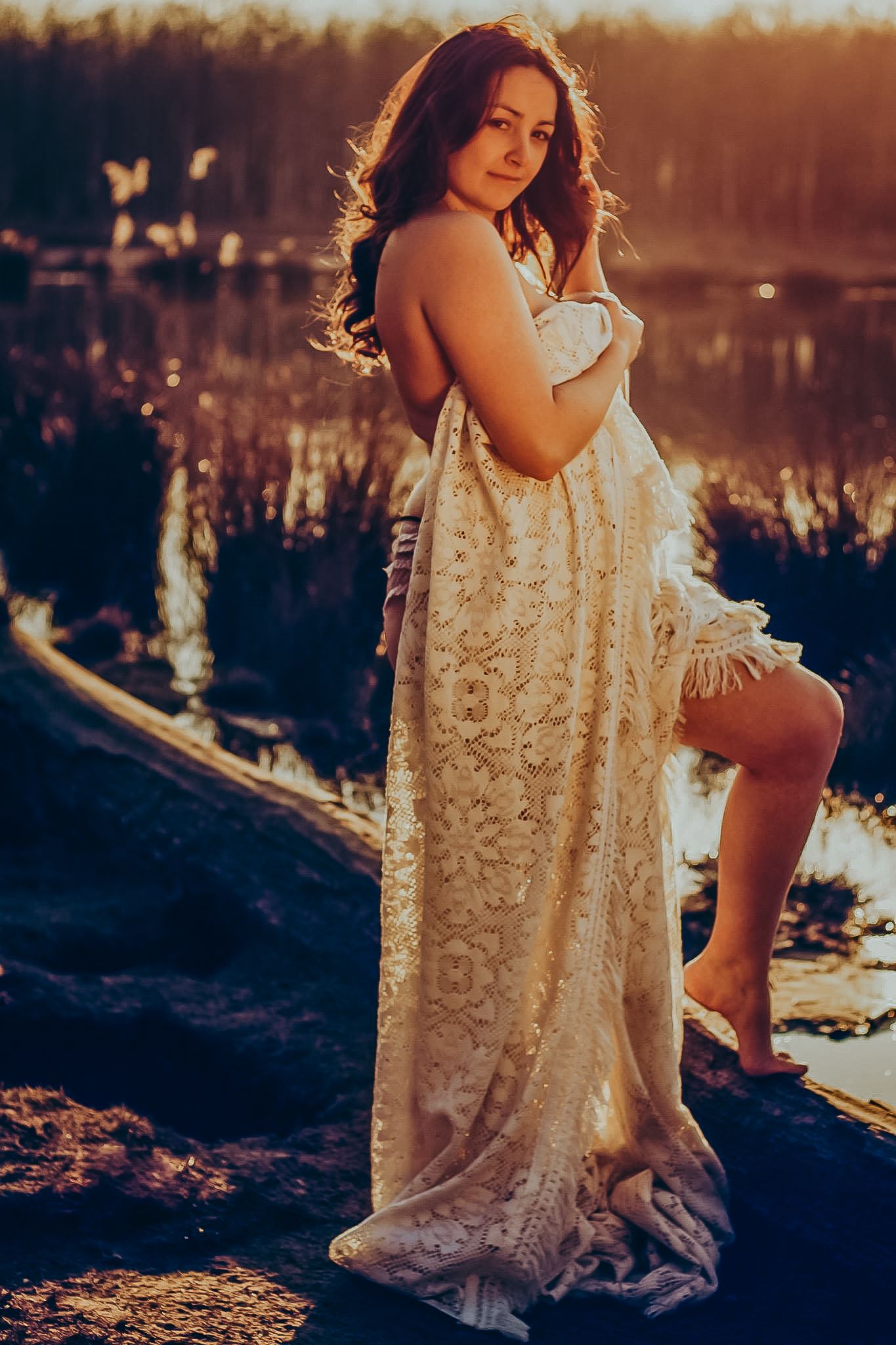 Romantic sunset photoshoot featuring a flowing lace dress against a lakeside backdrop.