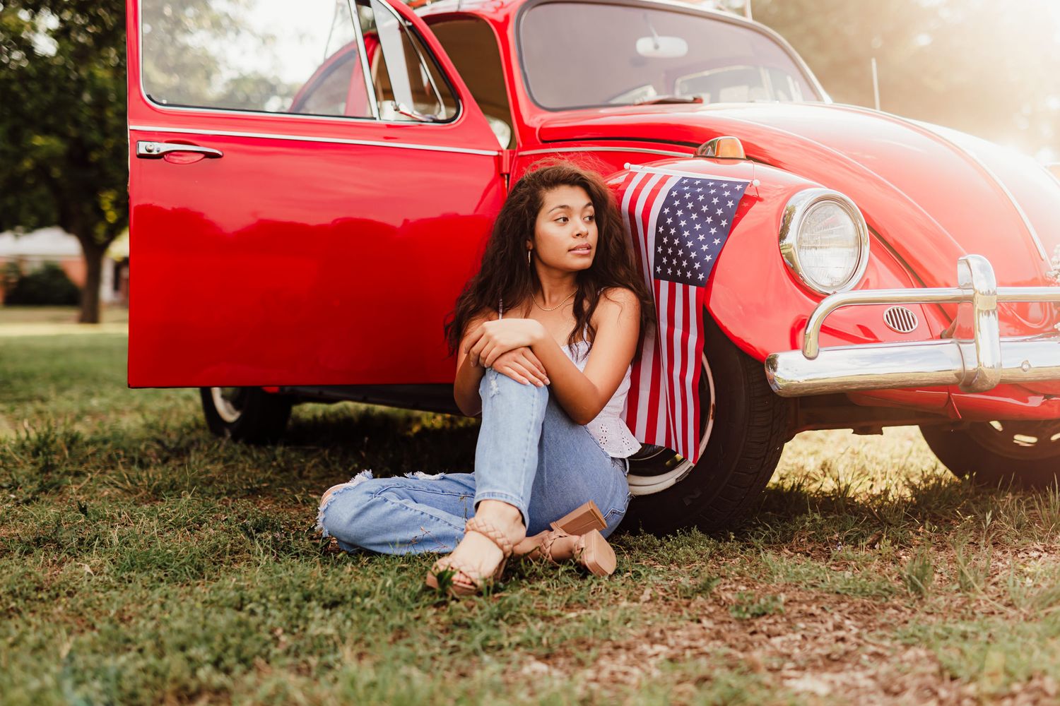 A red vintage Volkswagen Beetle with an American flag design parked on grass during golden hour.