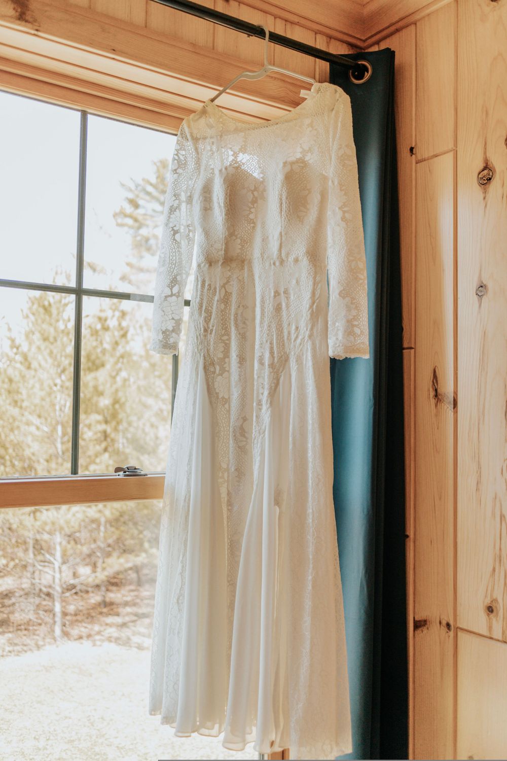White wedding dresses hanging in a rustic wooden room with natural light streaming through windows.