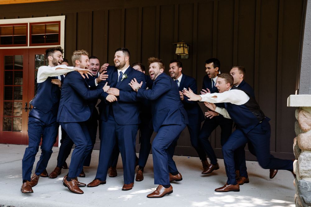 Wedding party in navy suits posing casually on wooden steps outdoors.