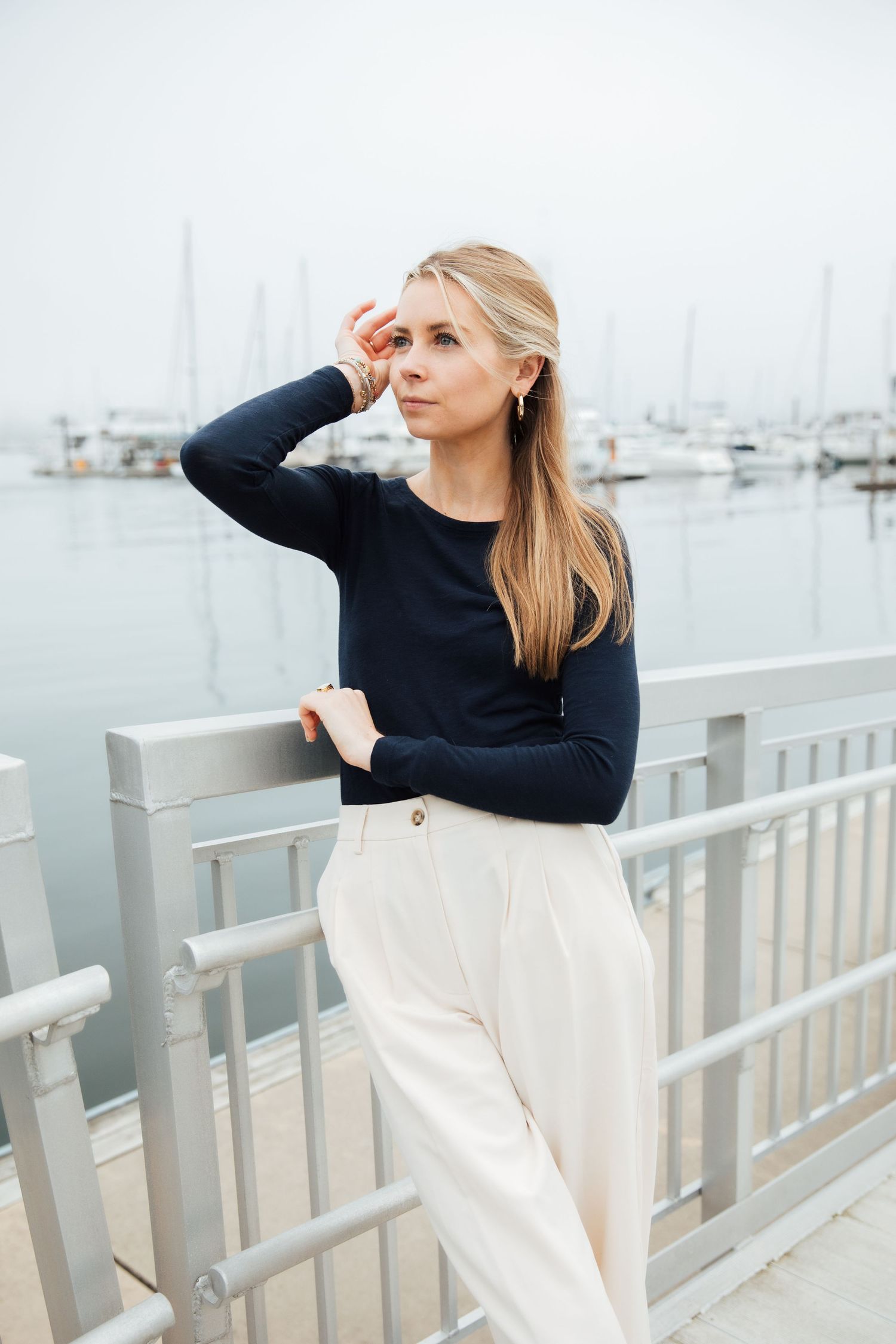 Woman in black sweater and white pants posing on dock with boats in background. branding photoshoot