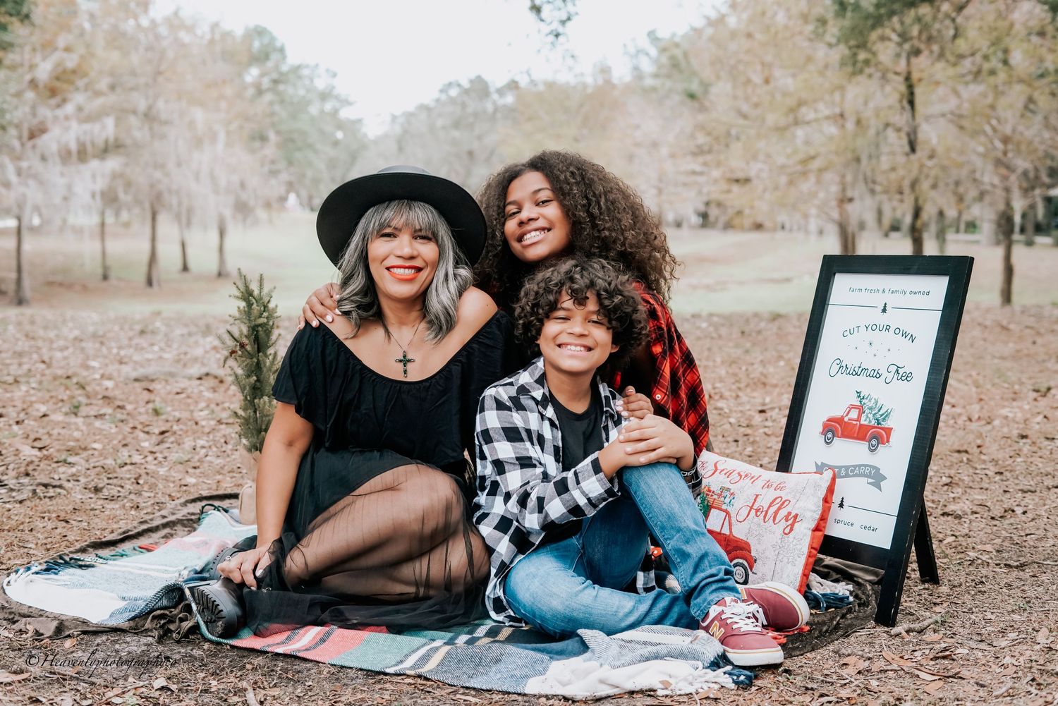 Three people sitting on picnic blanket outdoors with fall trees in background.