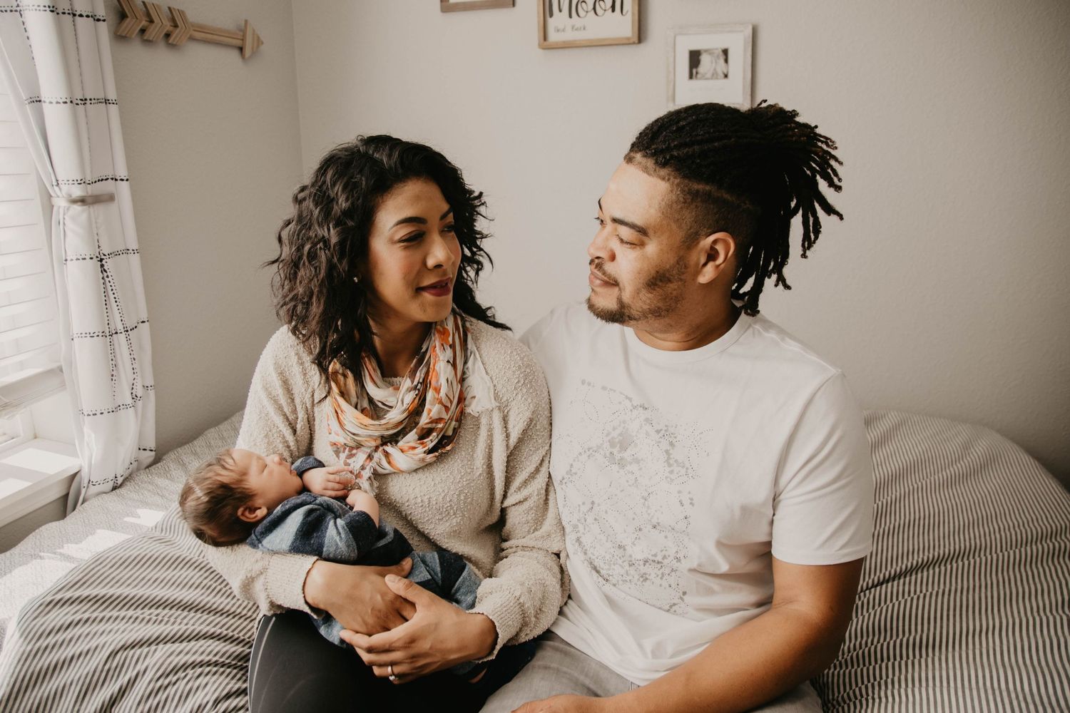 A couple shares a joyful moment while sitting together on gray bedding.