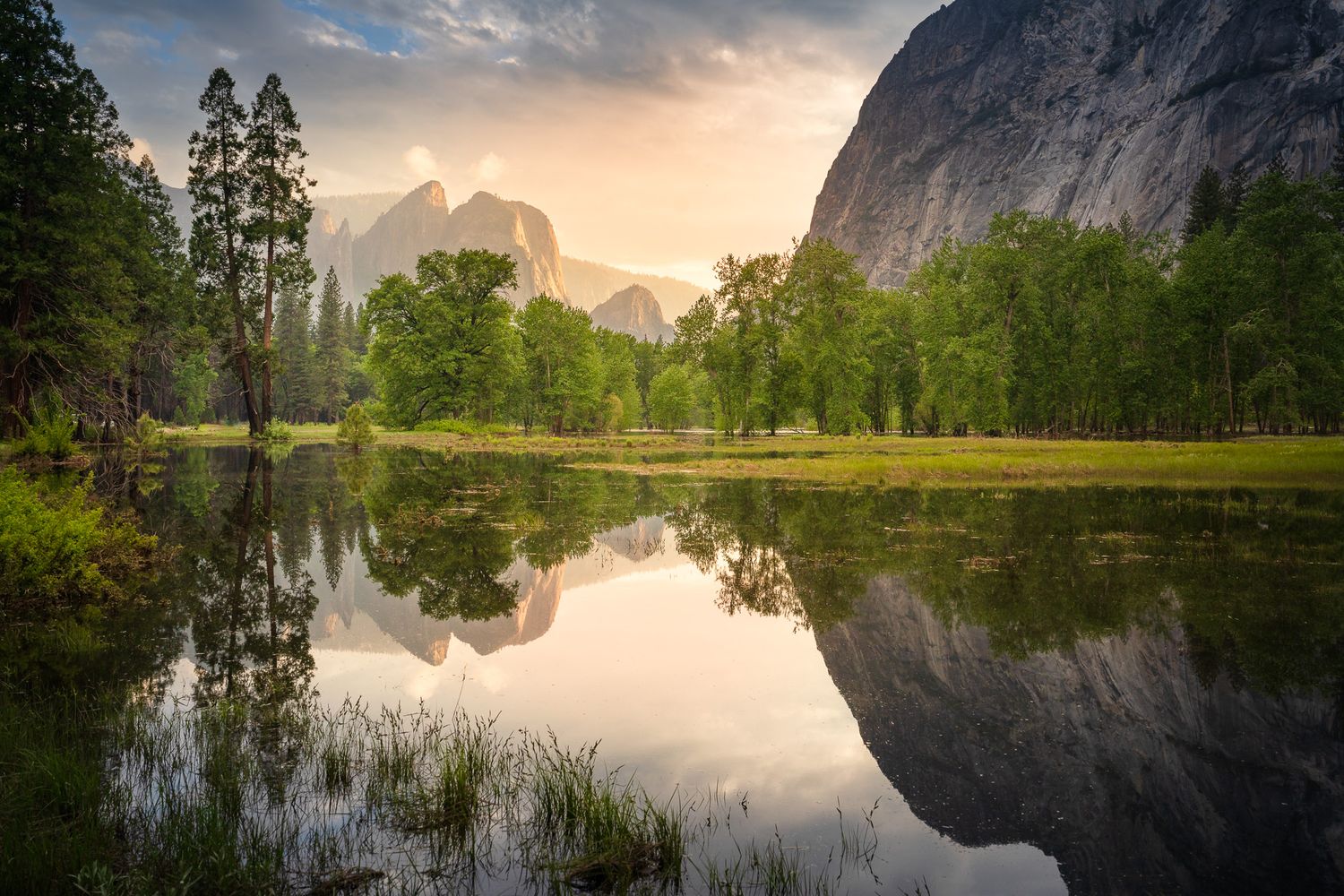 Misty sunset over a calm pond reflects towering granite cliffs and evergreen trees in Yosemite National Park.