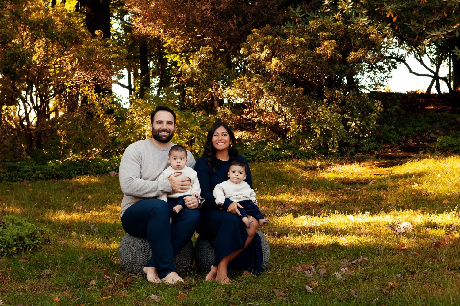 Family in navy outfits sits together on grass during golden autumn afternoon.