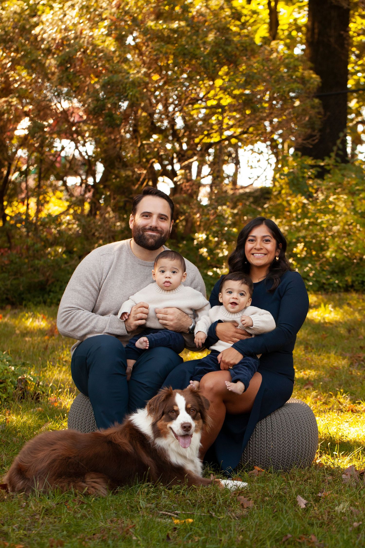 A family portrait outdoors in autumn with their brown and white border collie dog sitting in front of them.
