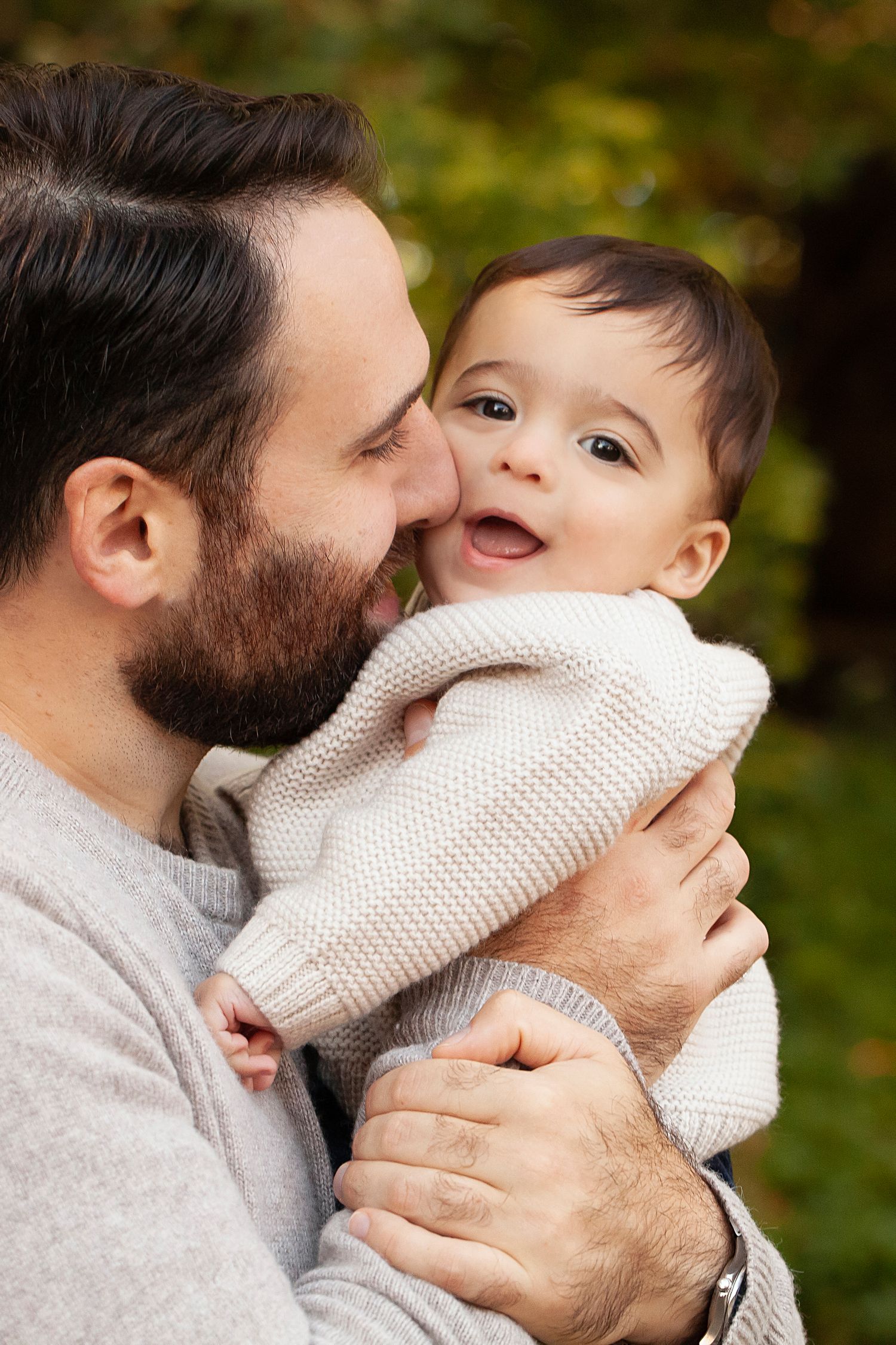 Intimate moment between parent and baby in cream sweater against autumn backdrop.