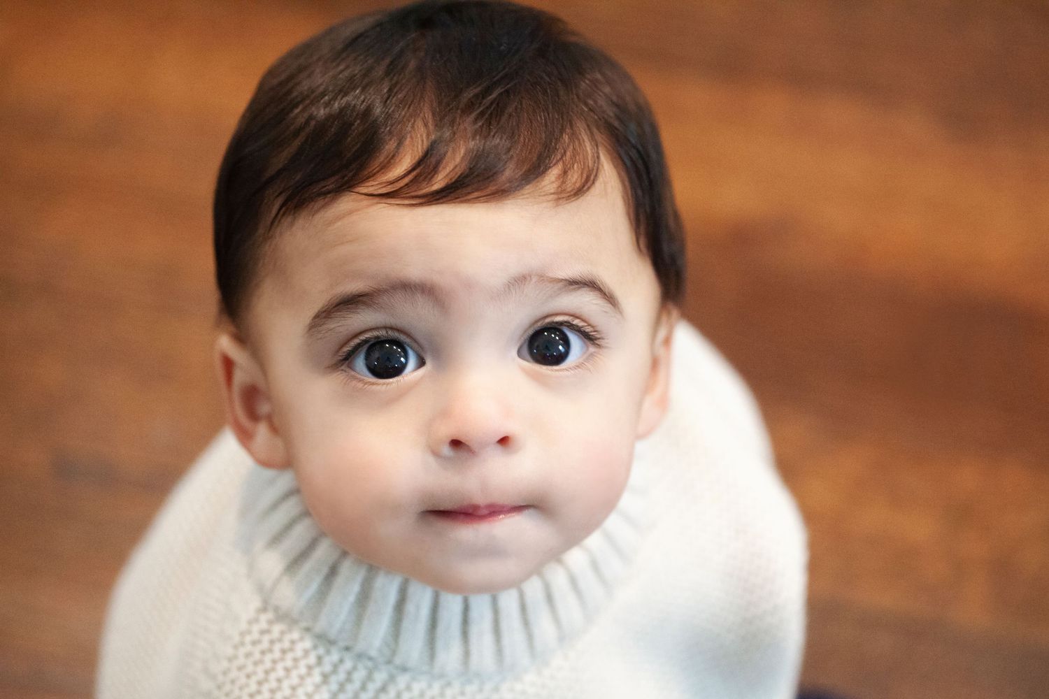 Close-up portrait of baby in cream sweater with big brown eyes.