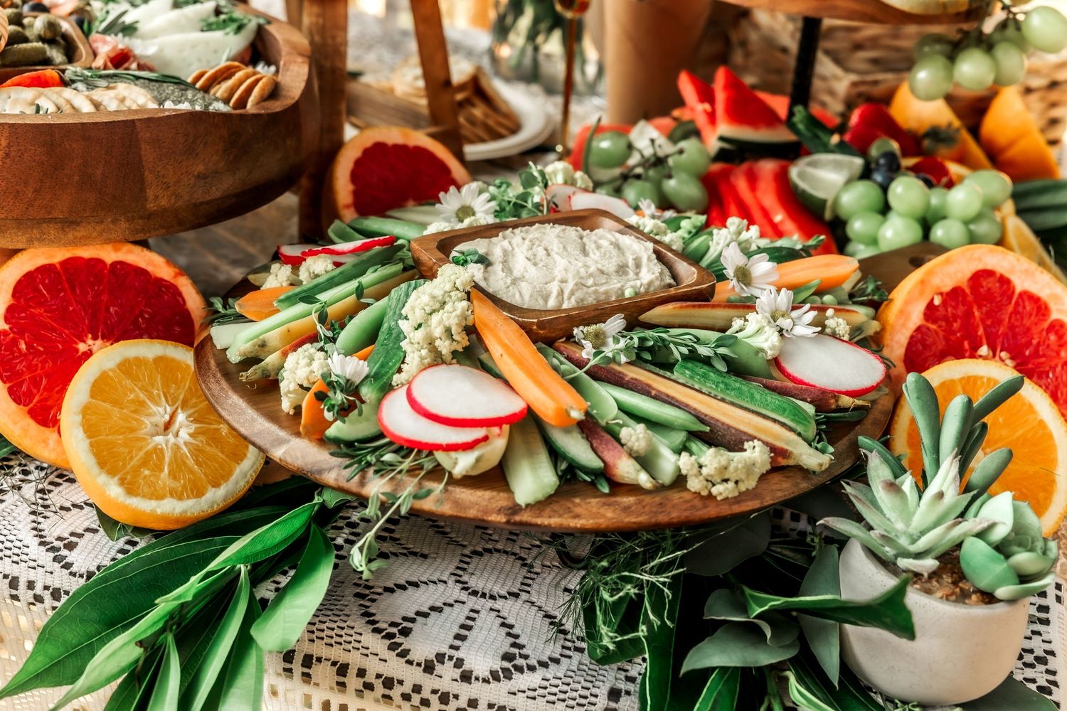 Fresh vegetable and fruit platter with citrus slices and herbs arranged on a lace tablecloth.