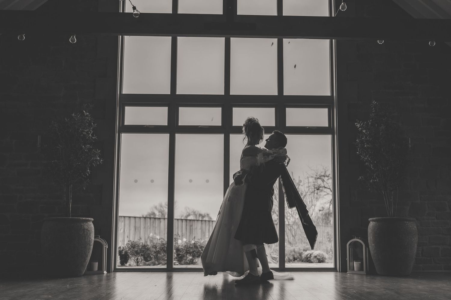 Black and white silhouette of couple dancing in front of large window.