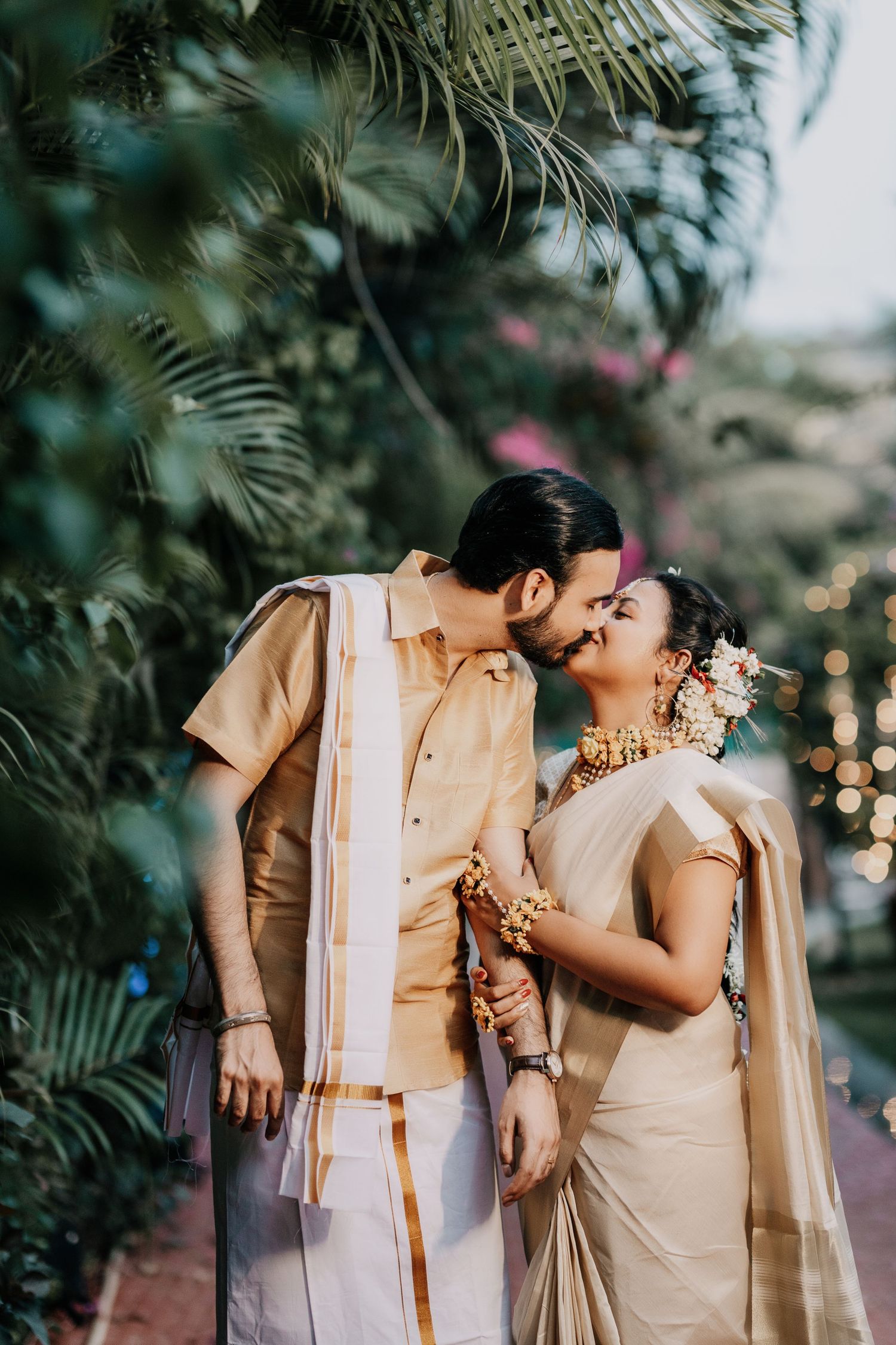 Romantic moment captured between couple in matching beige outfits surrounded by lush greenery.