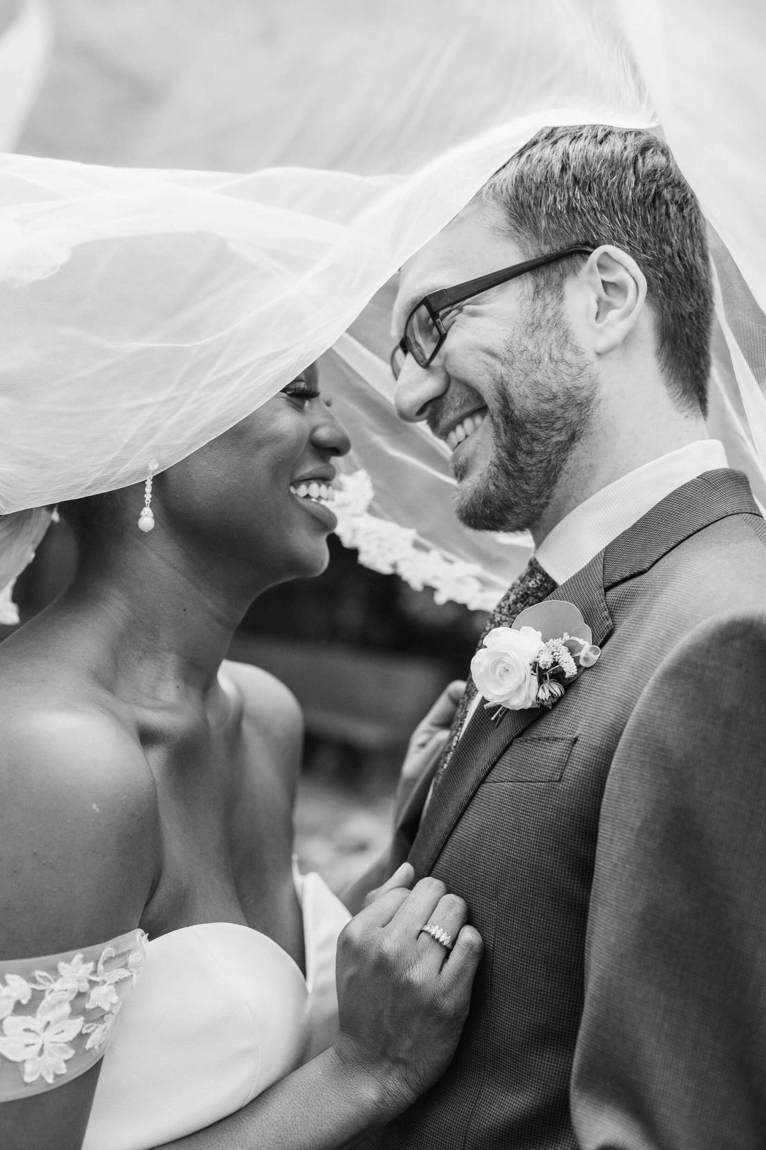 A romantic black and white wedding photo showing a tender moment under a flowing veil.