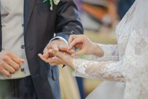 Delicate exchange of wedding rings between bride and groom's hands with lace sleeve details.