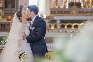 Tender moment between newlyweds in an ornate church setting with floral bouquet.