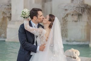 A wedding couple shares a romantic kiss in front of a historic fountain landmark in Rome.