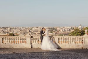 A wedding couple poses against a scenic city backdrop with ornate stone balustrades.