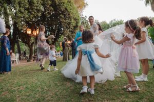 Children in formal attire play and dance during outdoor wedding festivities.