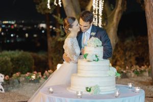 Elegant multi-tiered white wedding cake with floral decorations being cut by newlyweds during evening reception.