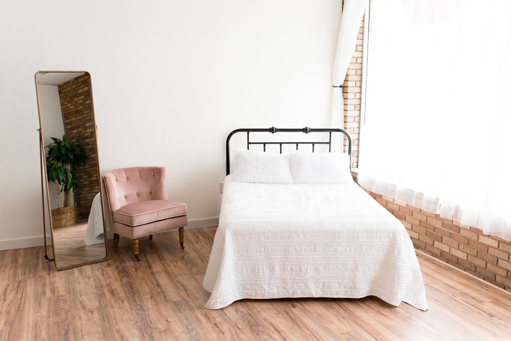 Bed setup with floor mirror and pink chair inside white and brick natural light photography studio
