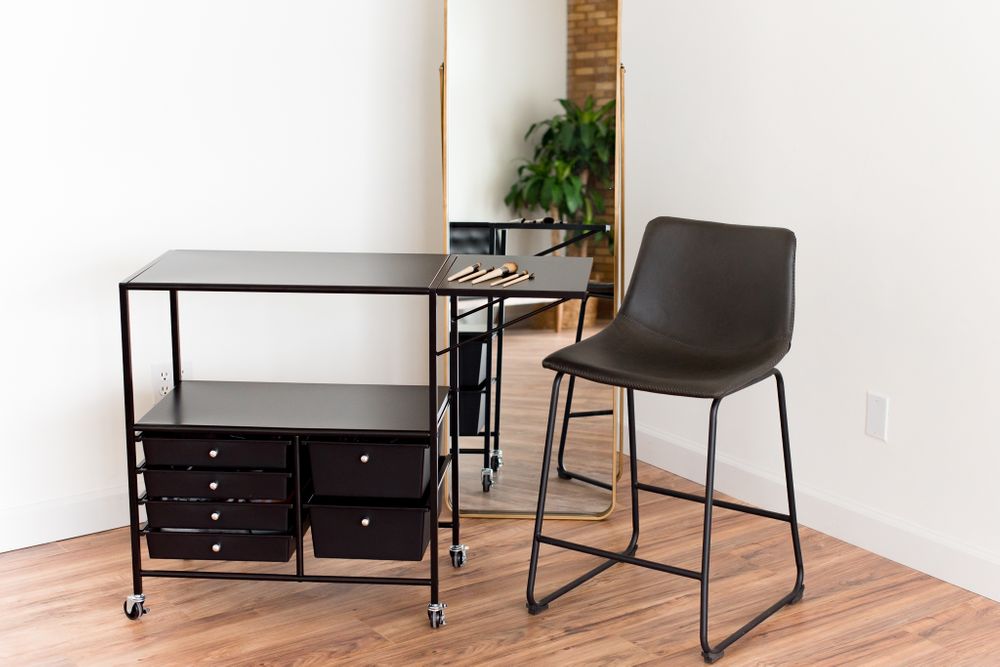 Mobile makeup station with black cart, stool, and floor mirror inside natural light photography studio