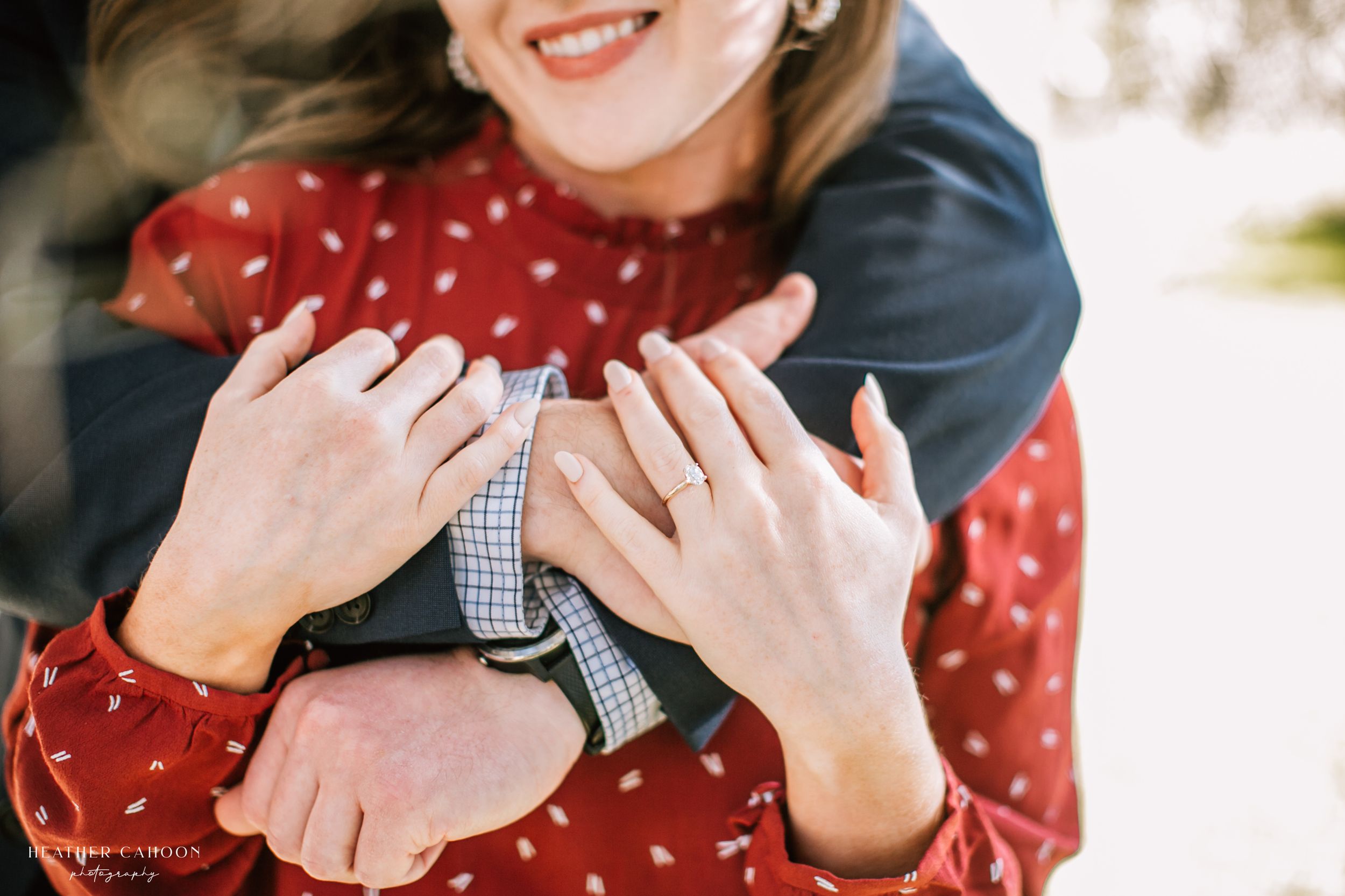 Close-up of embracing couple's hands showing affection while wearing red dot dress and navy sweater during engagement session in Hilton Head