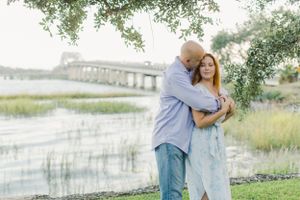 Couple photograph by waterfront in downtown Beaufort with bridge visible in background during sunset framed by the Beaufort trees and marsh
