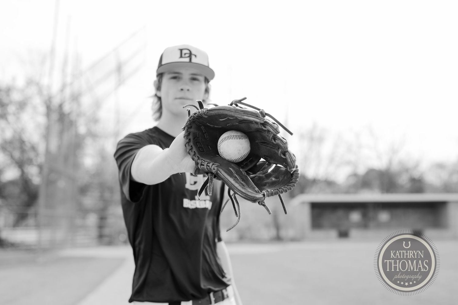 Baseball player in dark uniform holds up glove in black and white portrait shot.