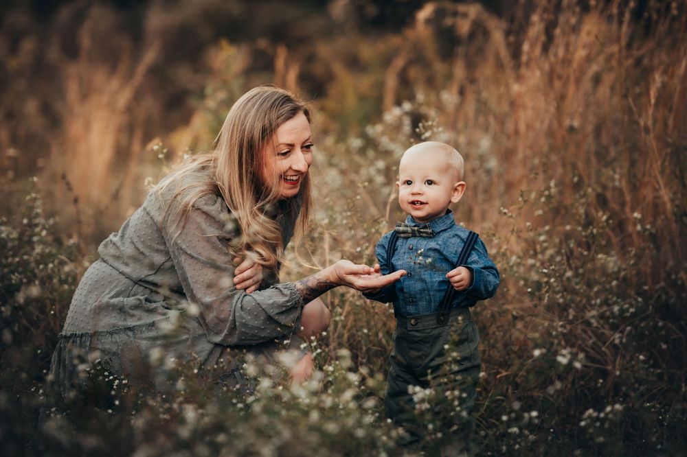 mother crouches down and holds out a flower for her toddler son to explore at Chattanooga fall mini sessions